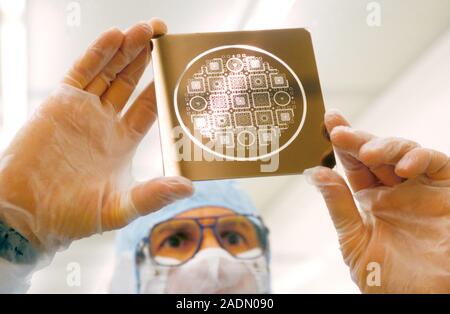 MEMS production. Clean room technician holding a silicon plate mask to be used to make MEMS (microelectromechanical systems) devices. MEMS devices are Stock Photo