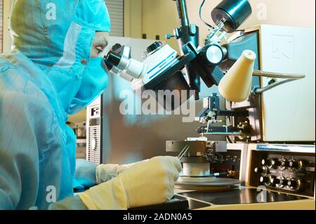 MODEL RELEASED. MEMS production. Clean room technician using a microscope as part of the process of adding the external connections to MEMS (microelec Stock Photo