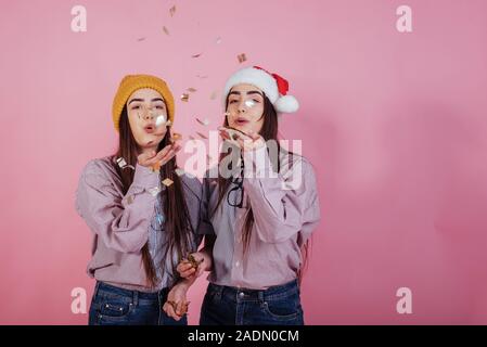 Finally holiday time. Giving air kiss using confetti. Two sisters twins standing and posing in the studio with white background Stock Photo