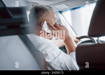 Silver colored phone. Having business call while sitting at the front of modern luxury car Stock Photo