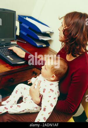 Laptop computing. Woman using a laptop computer at home, with her six-month-old son sitting on her lap and watching. Stock Photo