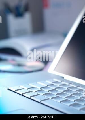 Laptop on a desk beside a compact disc (CD) and an open book. Stock Photo
