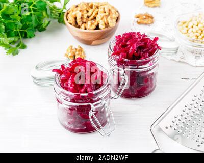 Fresh salad of grated boiled beetroot in glass jars, white wooden background, side view. Stock Photo
