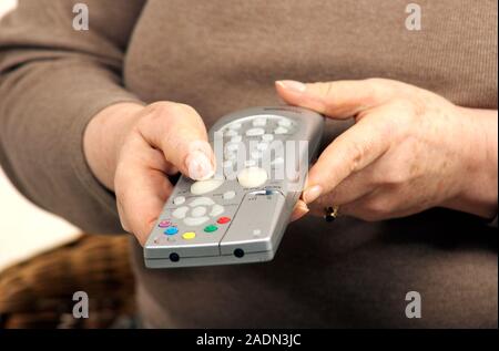 MODEL RELEASED. Remote control use. Woman pressing a button on a remote control. Stock Photo