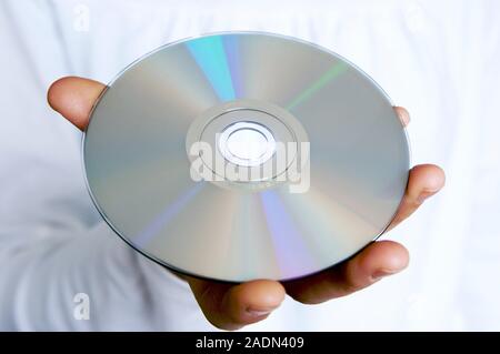 Compact disc (CD) being held in a hand. This is the correct way to hold a CD, as it cannot be played properly if its surface is scratched or dirty. Stock Photo