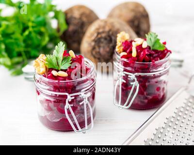 Fresh salad of grated boiled beetroot in glass jars, white wooden background, side view. Stock Photo