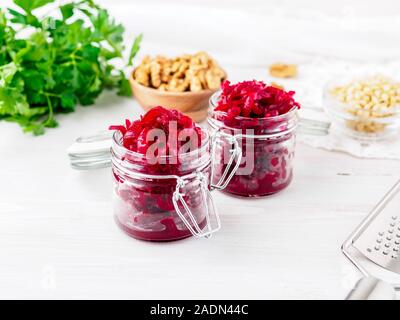 Fresh salad of grated boiled beetroot in glass jars, white wooden background, side view. Stock Photo