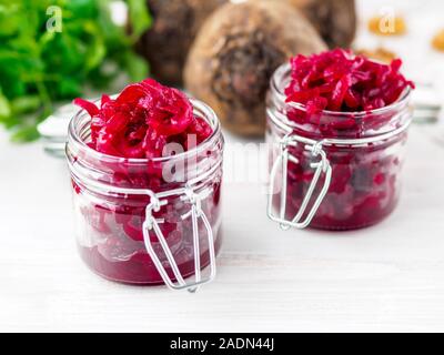 Fresh salad of grated boiled beetroot in glass jars, white wooden background, side view. Stock Photo