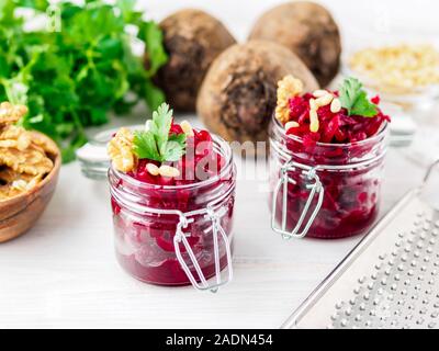 Fresh salad of grated boiled beetroot in glass jars, white wooden background, side view Stock Photo