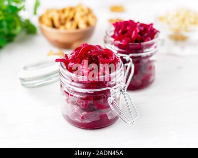 Fresh salad of grated boiled beetroot in glass jars, white wooden background, side view. Stock Photo