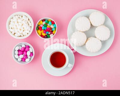 Cup of tea, plates of different sweets - marshmallows, lollipops, candy. Carbohydrates, glucose. Pink background Stock Photo