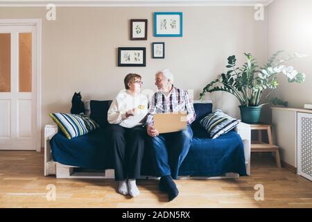 Elderly Caucasian couple doing shoppings online on the couch at home, looking at each other and smiling Stock Photo