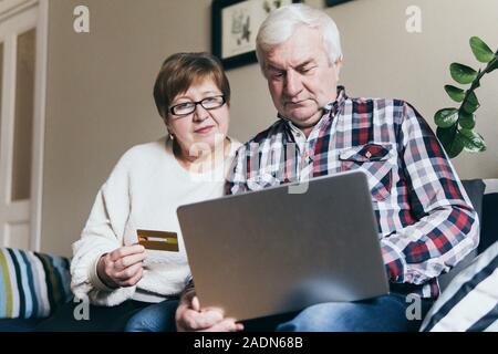 Elderly Caucasian couple doing shoppings online on the couch at home, looking at laptop screen and smiling Stock Photo