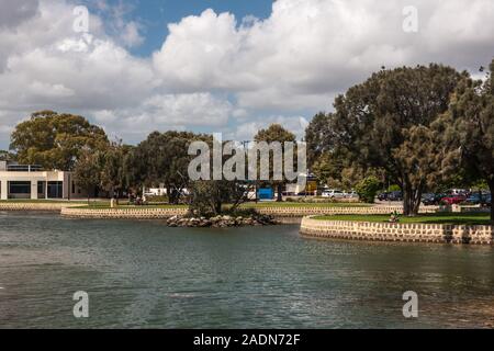 Mandurah, WA, Australia - November 25, 2009: Green park with trees and stone shoreline along channel waterway at The Boardwalk shopping mall. Greenish Stock Photo