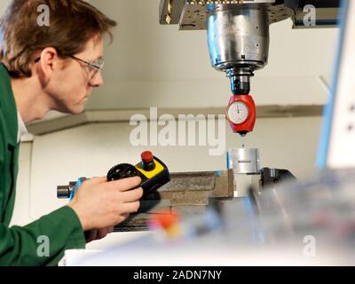 Metalwork. Metalworker using a 3D taster (red) to align the cutter of a CNC (computer numerical control) milling machine before use. The machine consi Stock Photo