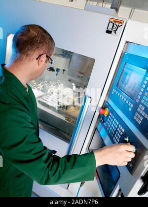 Metalwork. Metalworker operating a CNC (computer numerical control) milling machine (in background). The machine consists of a rotating cutter and a m Stock Photo