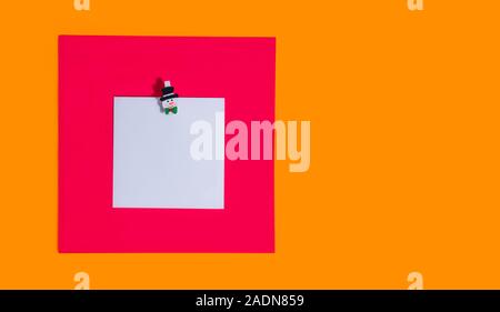 Blank square reminder memo note for writing ideas, things to do attached on a bright red and orange background with christmas decorative pin. Festive Stock Photo