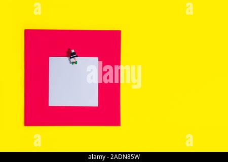 Blank square reminder memo note for writing ideas, things to do attached on a bright red and yellow background with christmas decorative pin. Festive Stock Photo