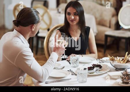 Table with salad, bread sticks and white plates. Beautiful couple have romantic dinner in luxury restaurant at evening time Stock Photo