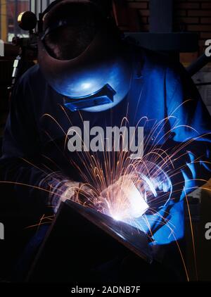 MODEL RELEASED. Welding. Worker using a welding torch to join two pieces of metal. He is wearing a heatproof visor and protective clothing to shield h Stock Photo