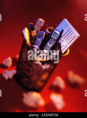 Obsolete technology. Mobile phones and a computer keyboard in a rubbish bin, representing outdated technology. Stock Photo