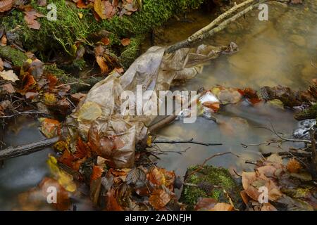 A plastic sheet polluting a woodland stream. Stock Photo
