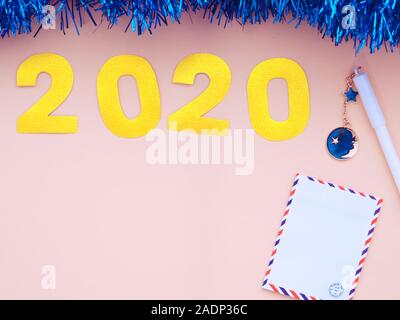 Blue garland on pink background with 2020 text on it, a letter and a pen. Feminine workspace background Stock Photo