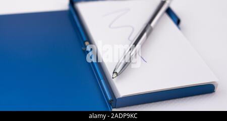 Hold a pen on a notebook to write down ideas and reminders on white paper and blue metal case Stock Photo