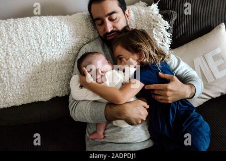 Exhausted dad on couch holding 4 yr old and newborn Stock Photo