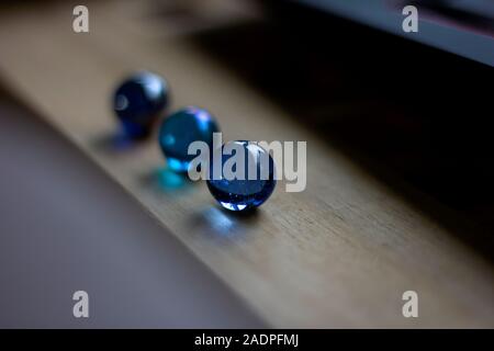 A portrait of three blue marbles, each having another shade of blue, on a wooden surface. Shining a bit of blue light onto the wood. Stock Photo