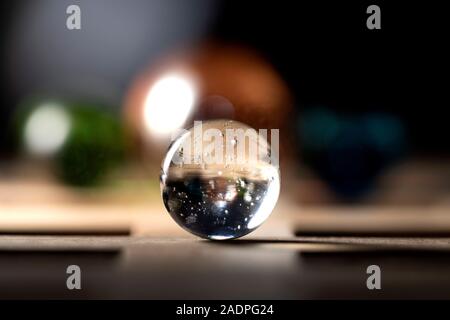 A close up portrait of a clear marble on a wooden surface with in the background three colored marbles in a nice bokeh blur. Stock Photo