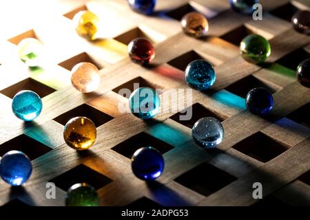 A portrait of multiple marbles all having a different color, lying on a wooden roster casting a colorful shadow onto the wooden surface. Stock Photo