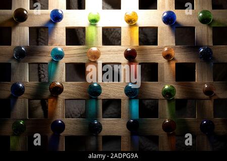 A top down portrait of multiple marbles all having a different color, lying on a wooden roster casting a colorful shadow onto the wooden surface. Stock Photo
