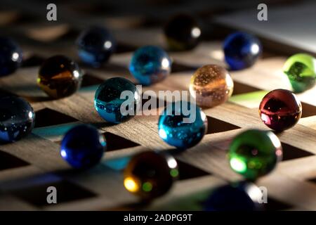 A portrait of a lot of different marbles in different colors, lying on a wooden roster casting a colorful shadow onto the wooden surface. Stock Photo