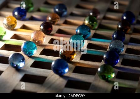 A portrait of a lot of different marbles in different colors, lying on a wooden roster casting a colorful reflection on to the wooden surface. Stock Photo