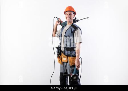 A builder with a hammer drill on his shoulder, and a angle grinder in his other hand, in a helmet, smiles. Stock Photo