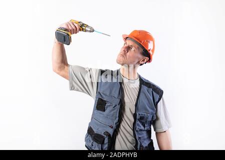 A builder in a helmet trying to drill his eye with a drill screwdriver. Stock Photo