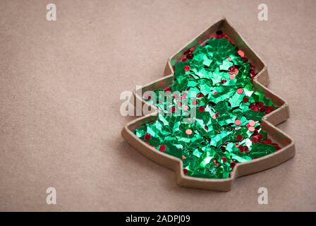 Cardboard Christmas tree outline filled with glittery holiday holly berries and leaves on an eco-friendly brown paper background Stock Photo