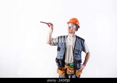 A builder in a helmet makes visual measurement with a marking pencil. Stock Photo