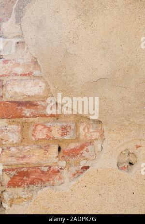 Close-up of an old, damaged & plastered beige wall. Plaster is partly peeled off revealing old bricks. High resolution full frame textured background. Stock Photo