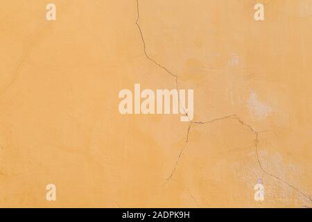 Close-up of a plastered concrete wall painted in orange. Plastering is cracked. High resolution full frame textured background. Stock Photo
