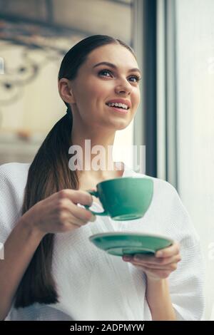 Positive long haired lady smiling and holding her cup Stock Photo
