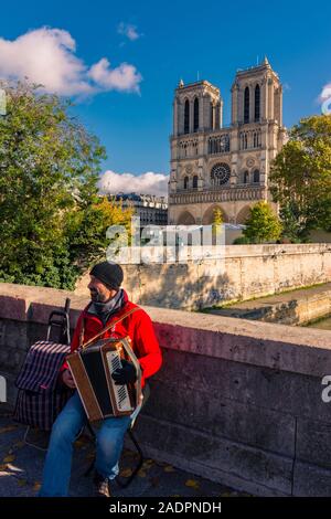 Paris, France - November 7, 2019: A street musician plays the accordion on the Des Coeurs bridge (of the Hearts) in front of the Notre Dame cathedral Stock Photo