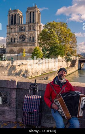 Paris, France - November 7, 2019: A street musician plays the accordion on the Des Coeurs bridge (of the Hearts) in front of the Notre Dame cathedral Stock Photo