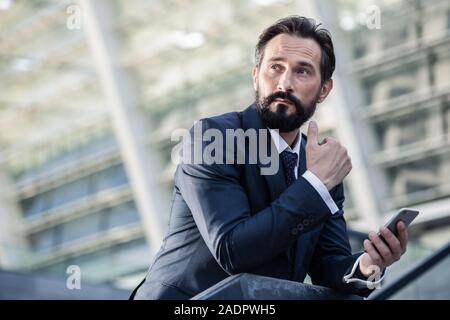 Thoughtful bearded businessman using his smartphone outdoors Stock Photo