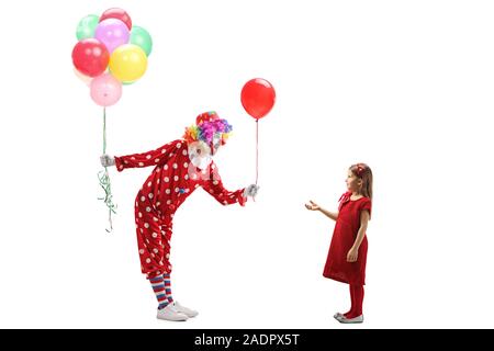 Full length profile shot of a clown with a bunch of balloons giving a red balloon to a little girl isolated on white background Stock Photo