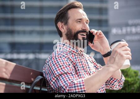 Waist up of a cheerful bearded man talking on phone outdoors Stock Photo