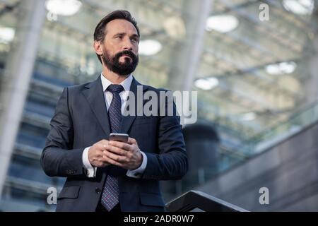 Waist up of a thoughtful bearded businessman using his smartphone Stock Photo