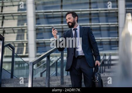 Delighted smiling businessman using his smartphone outdoors Stock Photo