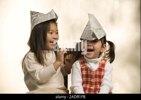 Portrait of two young Asian sisters wearing paper hats on a plain background Stock Photo